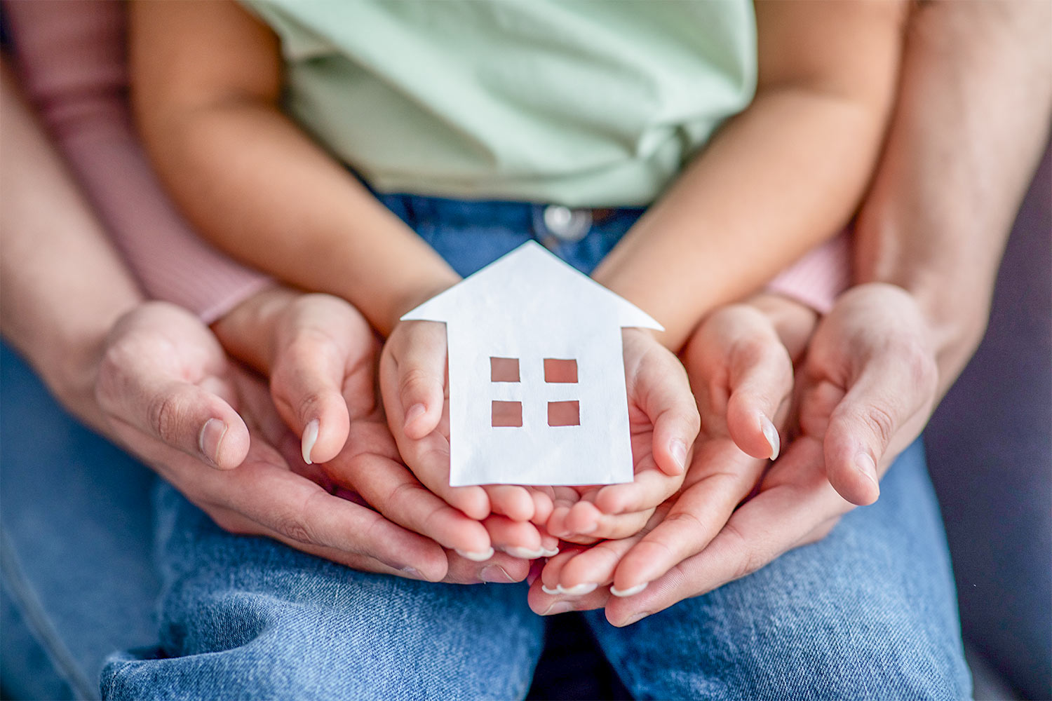 Man, woman and little child holding cutout paper house figure in hands